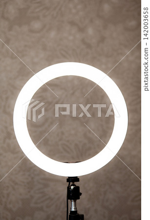 Circular LED ring light mounted on a stand, set against a textured background, suitable for enhancing lighting in photography and video production Circular LED ring light mounted on a stand, set against a textured background, suitable for enhancing lighting in photography and video production 142003658
