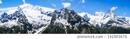 Snow-covered mountain peaks rise dramatically against a bright blue sky with fluffy clouds, showcasing the beauty of the alpine scenery Snow-covered mountain peaks rise dramatically against a bright blue sky with fluffy clouds, showcasing the beauty of the alpine scenery 142003678