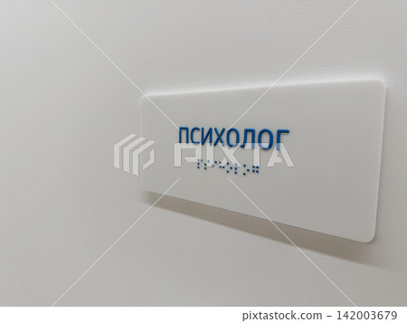Sign indicating psychologist office with Cyrillic text and Braille, mounted on a white wall, providing accessibility information for visitors Sign indicating psychologist office with Cyrillic text and Braille, mounted on a white wall, providing accessibility information for visitors 142003679