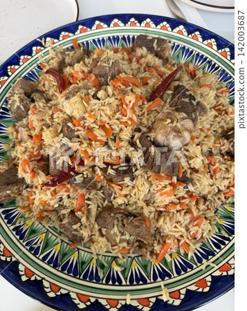 Traditional rice dish featuring beef, carrots, and spices, beautifully arranged on a decorative plate with colorful patterns and designs Traditional rice dish featuring beef, carrots, and spices, beautifully arranged on a decorative plate with colorful patterns and designs 142003687