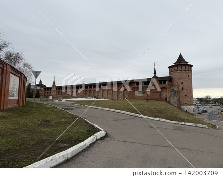 Kolomna, Russia - April 06, 2026: Historic red brick fortress features towers and walls alongside a curved road in a cloudy landscape with grass Kolomna, Russia - April 06, 2026: Historic red brick fortress features towers and walls alongside a curved road in a cloudy landscape with grass 142003709