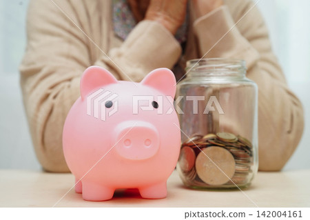 Retired elderly woman counting coins money with piggy bank and worry about monthly expenses and treatment fee payment. Retired elderly woman counting coins money with piggy bank and worry about monthly expenses and treatment fee payment. 142004161