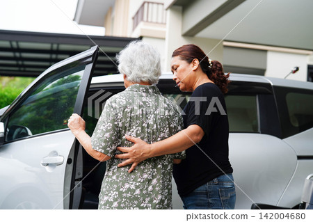 Caregiver help Asian elderly woman disability patient get in her car. 142004680