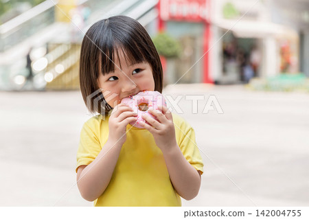 Happy Little Asian Girl Eating Pink Glazed Donut with Crumbs on Face, Sweet Snack and Childhood Joy 142004755