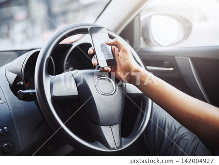 Person, texting and driving with phone on steering wheel with scroll, danger and risk. Road safety, awareness and driver in car with hand on smartphone, distraction and attention with auto insurance Person, texting and driving with phone on steering wheel with scroll, danger and risk. Road safety, awareness and driver in car with hand on smartphone, distraction and attention with auto insurance 142004927