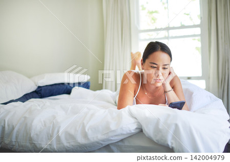 Phone, relax and Asian woman in bed on internet, social media or reading email in the morning in home. Smartphone, bedroom and serious person on app, blog and scroll on mobile technology in house Phone, relax and Asian woman in bed on internet, social media or reading email in the morning in home. Smartphone, bedroom and serious person on app, blog and scroll on mobile technology in house 142004979