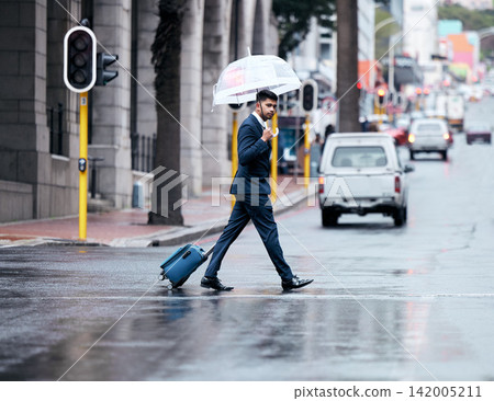 Businessman, walking and city with umbrella on street for travel, work or business trip in winter. Man, employee or pedestrian crossing road with luggage for commute or immigration in an urban town Businessman, walking and city with umbrella on street for travel, work or business trip in winter. Man, employee or pedestrian crossing road with luggage for commute or immigration in an urban town 142005211