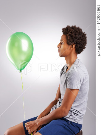 Black man, balloon and thinking in studio for mental health with sad, green and unhappy. Male person, problem and sphere by grey background for anxiety with frustrated, negative attitude and moody 142005662