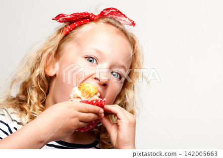 Eating, cupcake and portrait of child in studio for dessert, sweet treat or sugar snack with white background. Bite, tasting and girl with vanilla cake for confection, hungry and enjoy delicious food Eating, cupcake and portrait of child in studio for dessert, sweet treat or sugar snack with white background. Bite, tasting and girl with vanilla cake for confection, hungry and enjoy delicious food 142005663