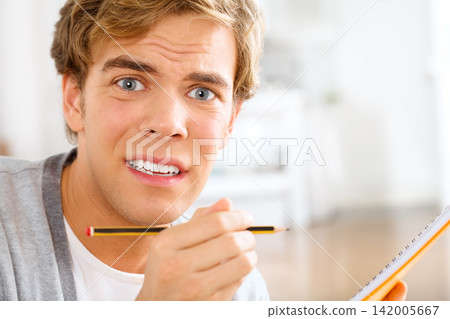 Portrait, confused and man writing notes in classroom for studying, learning or knowledge in notebook. Student, education and male person with pencil for project, exam or university assignment 142005667