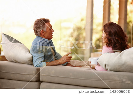 Patio, mature couple and talking with coffee, sofa and outdoor for discussion, pointing and together. Home, man and woman on couch, love and drink in morning, speaking and relationship of marriage Patio, mature couple and talking with coffee, sofa and outdoor for discussion, pointing and together. Home, man and woman on couch, love and drink in morning, speaking and relationship of marriage 142006068