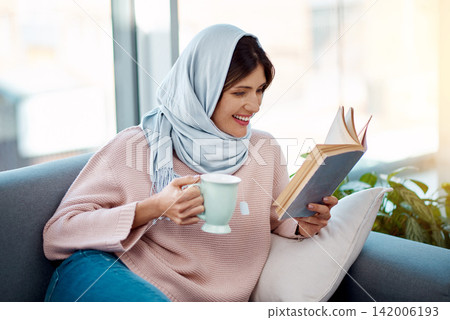 Relax, reading and muslim woman with coffee and book on sofa in living room at home. Smile, cappuccino and islamic female person resting and enjoying literature, novel or story on couch at apartment. 142006193