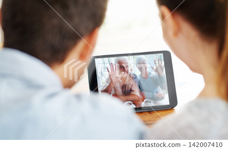 Happy couple, tablet and video call with grandparents for greeting or online conversation at home. Rear view of man and woman talking or waving with technology for virtual meeting or communication Happy couple, tablet and video call with grandparents for greeting or online conversation at home. Rear view of man and woman talking or waving with technology for virtual meeting or communication 142007410