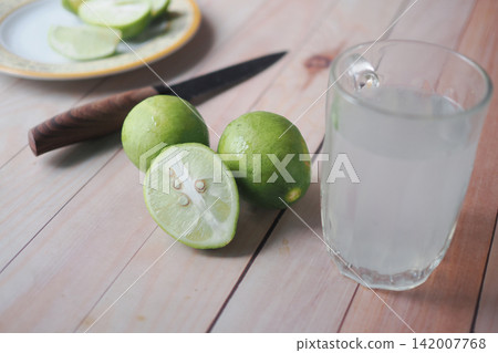 Slicing limes beside a glass of lime drink on wooden table Slicing limes beside a glass of lime drink on wooden table 142007768