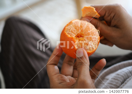 Hand holding a peeled orange over a person's lap Hand holding a peeled orange over a person's lap 142007776