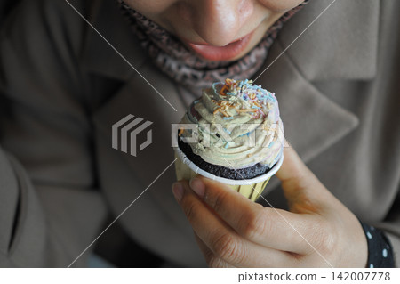 Enjoying a cupcake with colorful frosting in a cafe Enjoying a cupcake with colorful frosting in a cafe 142007778