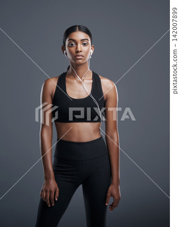 Indian woman, portrait and headphones in studio for music, listening and fitness by dark background. Gen z athlete, streaming and audio for workout, sports and training with podcast or playlist Indian woman, portrait and headphones in studio for music, listening and fitness by dark background. Gen z athlete, streaming and audio for workout, sports and training with podcast or playlist 142007899