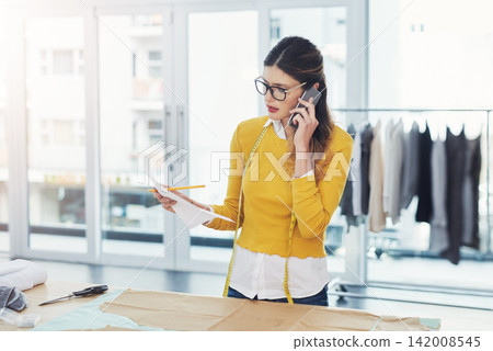 Fashion, business and woman with phone call for logistics, delivery and planning order shipping. Tailor, client and contact warehouse for manufacturing info, problem solving or employee in workshop Fashion, business and woman with phone call for logistics, delivery and planning order shipping. Tailor, client and contact warehouse for manufacturing info, problem solving or employee in workshop 142008545