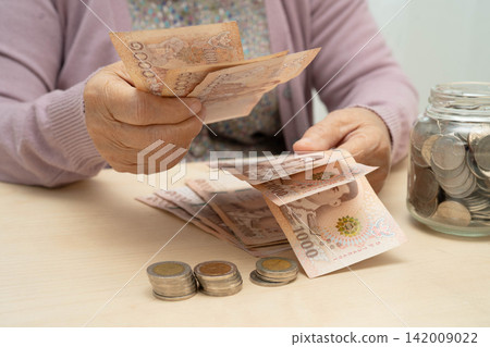 Retired Asian elderly woman counting coins money and worry about monthly expenses and treatment fee payment. Retired Asian elderly woman counting coins money and worry about monthly expenses and treatment fee payment. 142009022