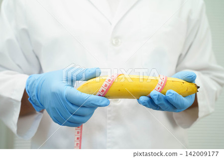 Male doctor stands holding a banana, penis health. Male doctor stands holding a banana, penis health. 142009177