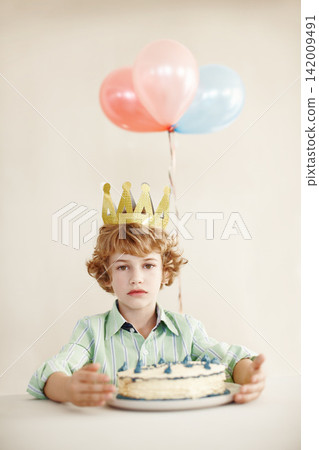 Birthday cake, portrait and balloons with sad boy by table in family home for celebration, growth and lonely. Dessert, decoration and sweet pastry for event, serious and milestone with crown in house Birthday cake, portrait and balloons with sad boy by table in family home for celebration, growth and lonely. Dessert, decoration and sweet pastry for event, serious and milestone with crown in house 142009491