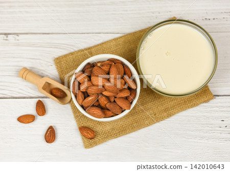 Almond milk in bowl and almonds on wooden scoop on sack 142010643