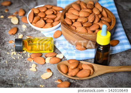 Almond oil and Almonds nuts on bowl dark background, Delicious sweet almonds oil in glass bottle, roasted almond nut for healthy food and snack organic vegetable oils for cooking or spa Almond oil and Almonds nuts on bowl dark background, Delicious sweet almonds oil in glass bottle, roasted almond nut for healthy food and snack organic vegetable oils for cooking or spa 142010649