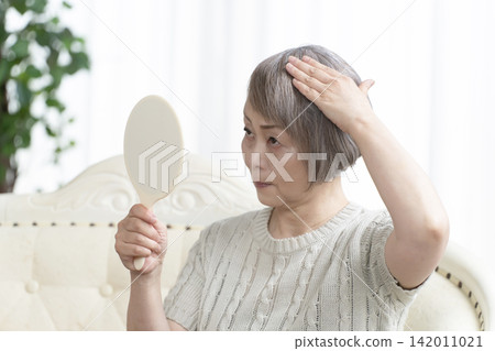 A senior woman holding a hand mirror in her living room 142011021