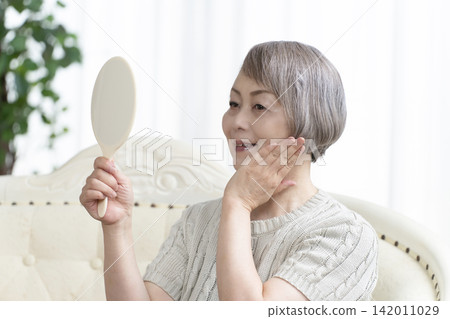 一位老婦人在客廳拿著一面手鏡。 一位老婦人在客廳拿著一面手鏡。 142011029