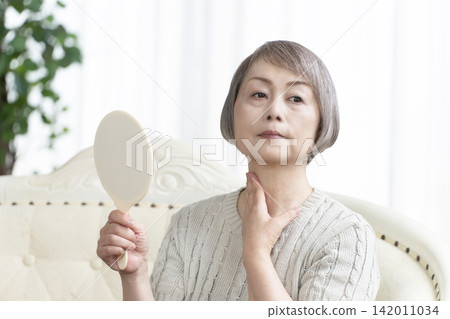 一位老婦人在客廳拿著一面手鏡。 一位老婦人在客廳拿著一面手鏡。 142011034