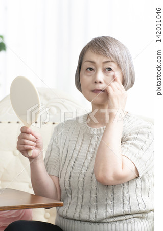 一位老婦人在客廳拿著一面手鏡。 一位老婦人在客廳拿著一面手鏡。 142011046