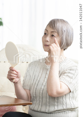 A senior woman holding a hand mirror in her living room 142011047
