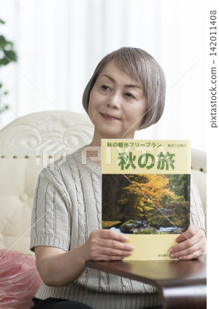 A senior woman is looking at a travel magazine on the living room sofa. A senior woman is looking at a travel magazine on the living room sofa. 142011408
