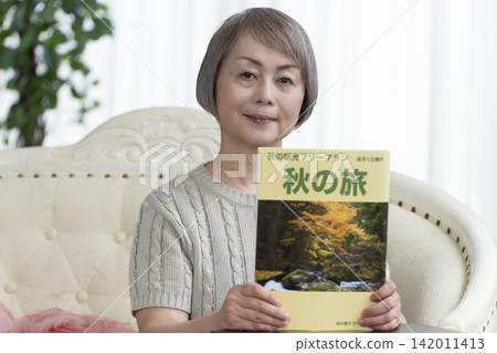 A senior woman is looking at a travel magazine on the living room sofa. A senior woman is looking at a travel magazine on the living room sofa. 142011413