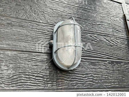 Marine-style weatherproof wall-mounted lighting fixtures, installed on a black wood-grain exterior wall. Marine-style weatherproof wall-mounted lighting fixtures, installed on a black wood-grain exterior wall. 142012001