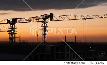 Construction cranes silhouetted against a vibrant sunset sky Construction cranes silhouetted against a vibrant sunset sky 142013287