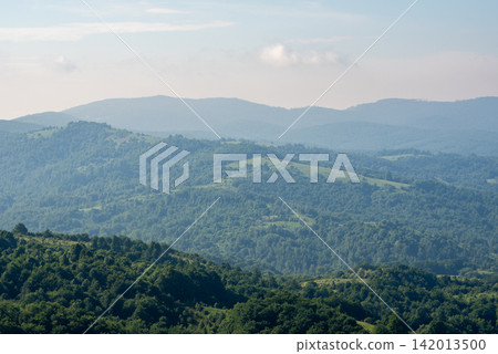 A panoramic view of a vast mountainous landscape from high elevation, dominated by dense forests and open fields in the foreground A panoramic view of a vast mountainous landscape from high elevation, dominated by dense forests and open fields in the foreground 142013500
