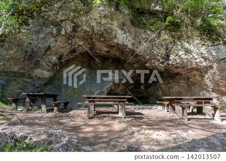 A rustic outdoor scene with a rocky backdrop featuring wooden picnic tables and benches A rustic outdoor scene with a rocky backdrop featuring wooden picnic tables and benches 142013507