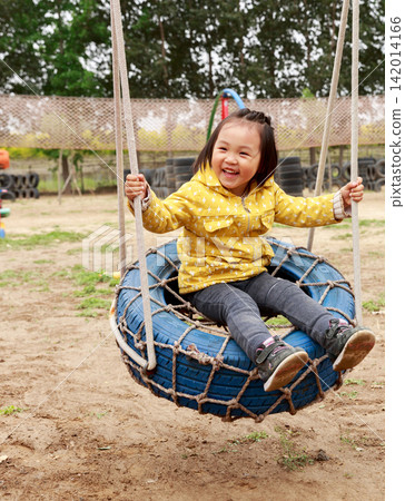 Happy little Asian girl laughing while playing on a blue tire swing at the park, joyful childhood moments and outdoor recreation. Happy little Asian girl laughing while playing on a blue tire swing at the park, joyful childhood moments and outdoor recreation. 142014166