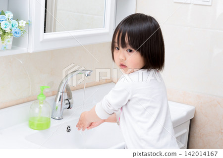 Small child washing hands with soap at the bathroom sink for hygiene 142014167