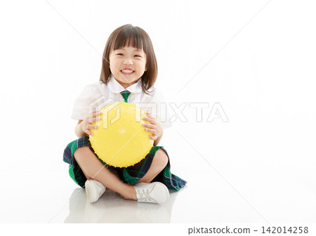 Happy Asian school girl sitting on floor holding a yellow sensory ball, physical education and play concept. Happy Asian school girl sitting on floor holding a yellow sensory ball, physical education and play concept. 142014258