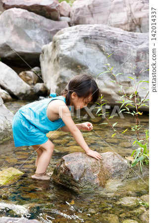Little girl in blue dress playing with water by the rocky creek alone Little girl in blue dress playing with water by the rocky creek alone 142014337