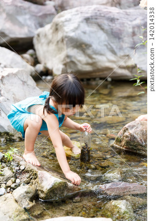 Little girl in blue dress playing with water by the rocky creek alone Little girl in blue dress playing with water by the rocky creek alone 142014338