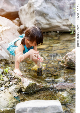 Little girl in blue dress playing with water by the rocky creek alone 142014339