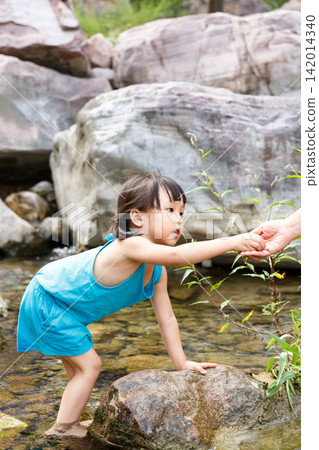 Little girl in blue dress playing with water by the rocky creek alone Little girl in blue dress playing with water by the rocky creek alone 142014340