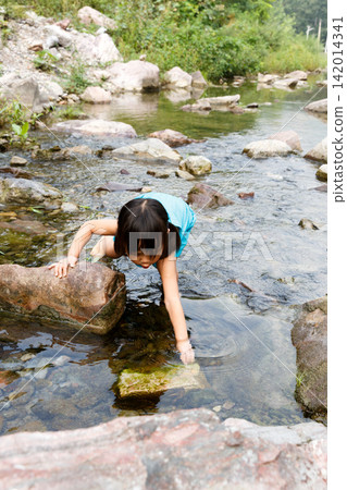 Little girl in blue dress playing with water by the rocky creek alone Little girl in blue dress playing with water by the rocky creek alone 142014341