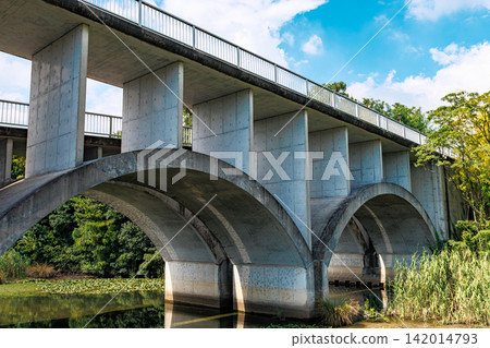 A beautiful arched concrete bridge surrounded by blue skies and lush greenery. A beautiful arched concrete bridge surrounded by blue skies and lush greenery. 142014793