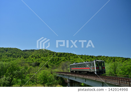 一列火車在湛藍的天空下,沿著豆谷本線行駛,周圍綠樹環繞。 一列火車在湛藍的天空下,沿著豆谷本線行駛,周圍綠樹環繞。 142014998