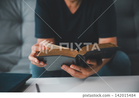 Close-up of an adult woman holding and reading an old Holy Bible at home, representing Christian faith, scripture study, devotion, spiritual guidance, wisdom, and hope. Close-up of an adult woman holding and reading an old Holy Bible at home, representing Christian faith, scripture study, devotion, spiritual guidance, wisdom, and hope. 142015484