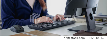 Young Asian furniture designer typing on computer while reviewing material samples and color swatches at modern studio desk Young Asian furniture designer typing on computer while reviewing material samples and color swatches at modern studio desk 142018162